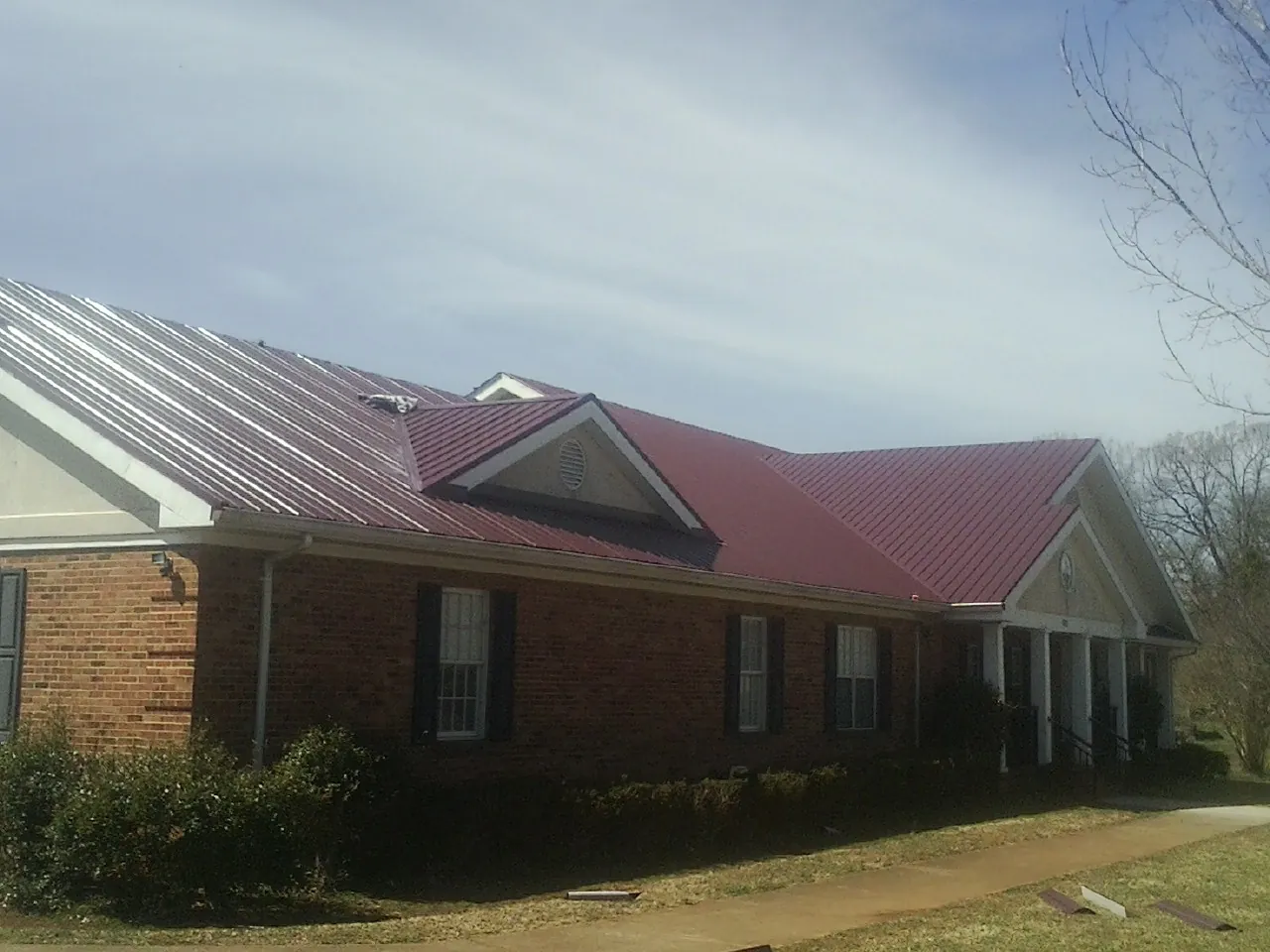 Red metal roof with gabled entries on a long brick building, from a Hail Damage Roof Repair job in Buffalo Valley