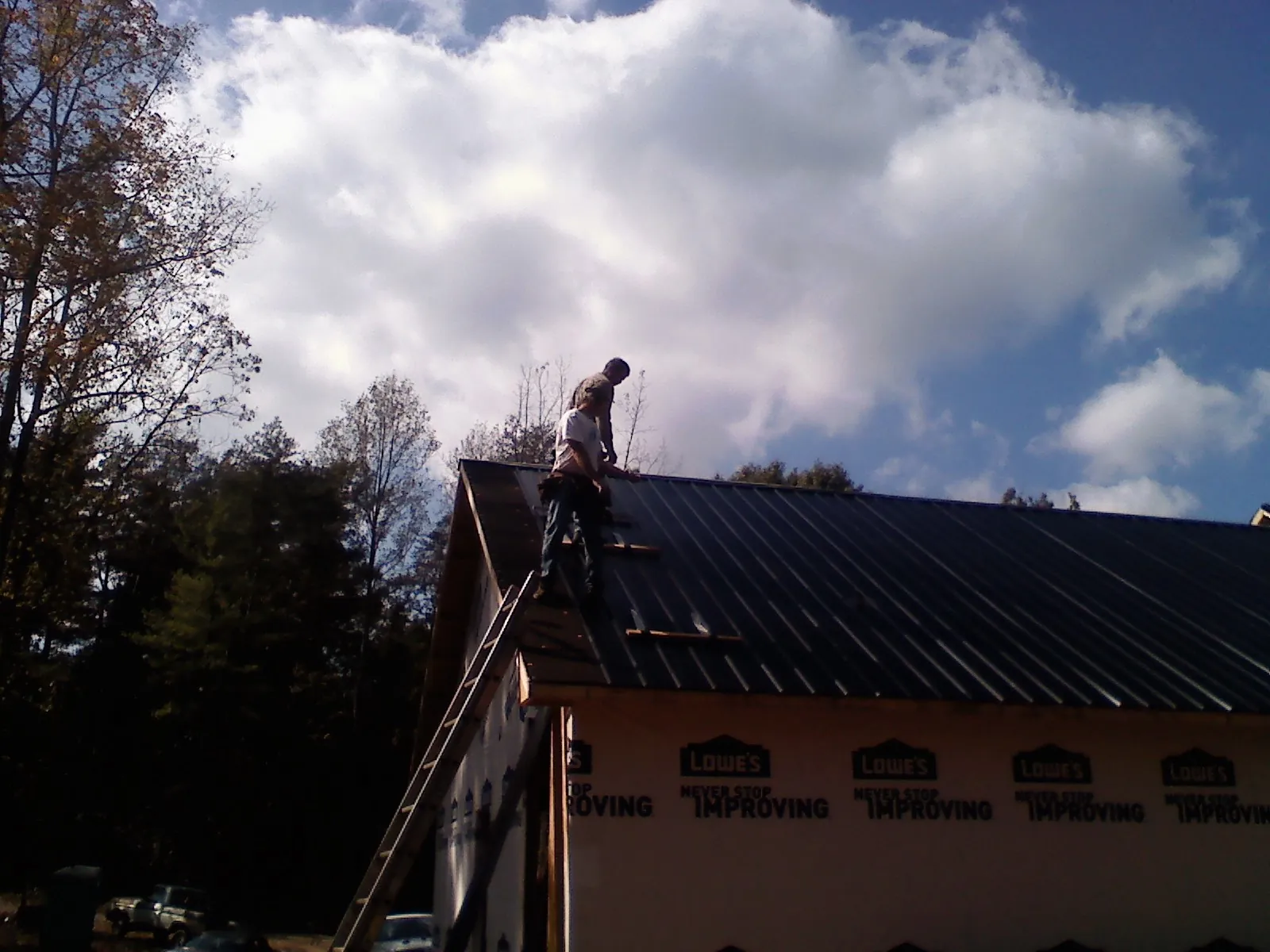 Roofer fastening dark metal panels high against a cloudy sky, from a Roof Inspection job in Buffalo Valley