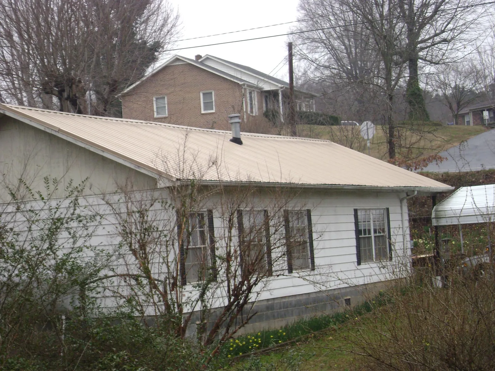 Tan metal roof on a white sided house set into a hillside — Commercial Roofing by Roofing Brothers in Buffalo Valley