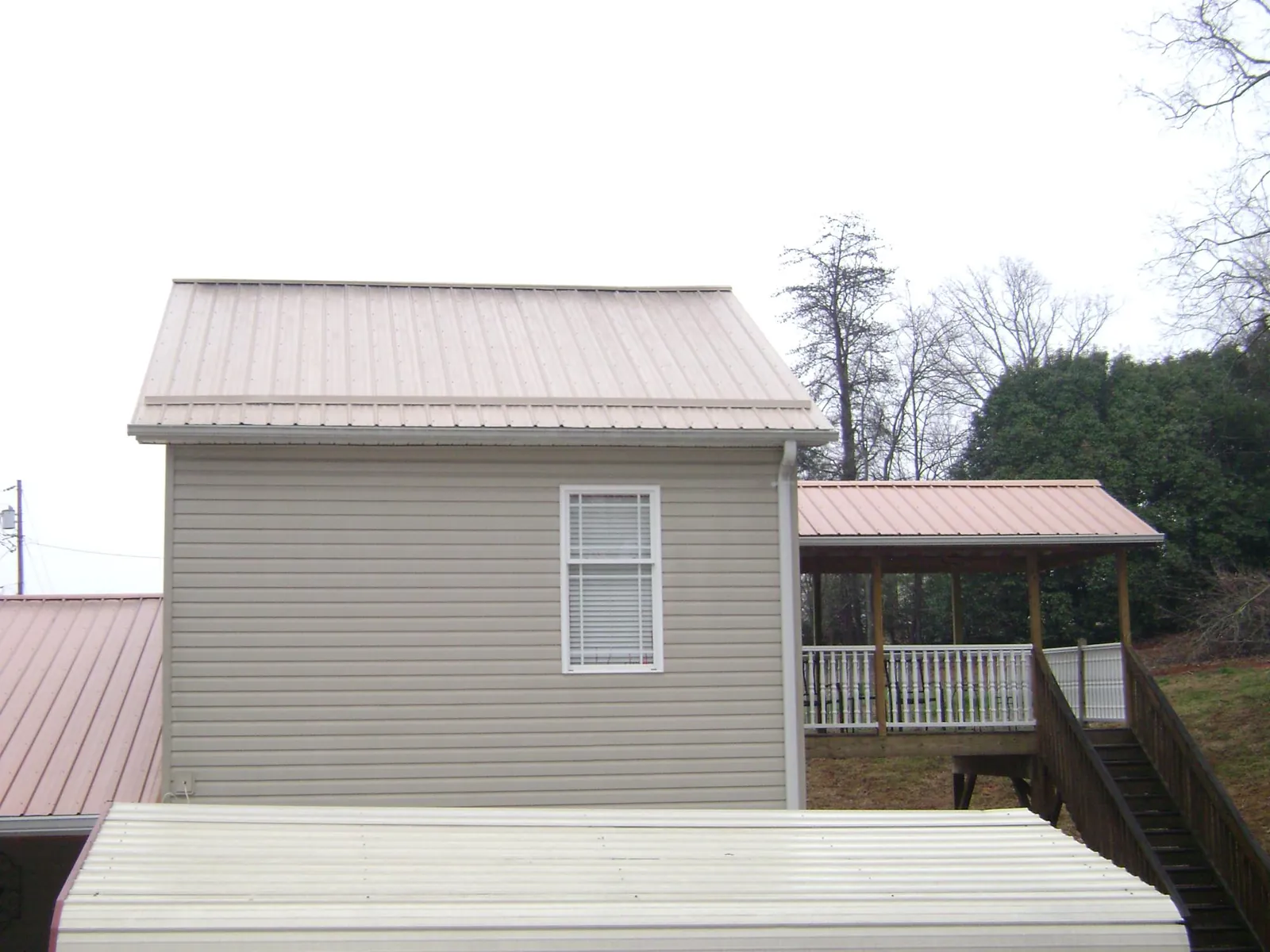 Tan metal roofs on a two story addition and attached porch, from a Roof Replacement job in Buffalo Valley